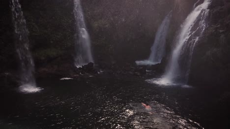 disparo de dron de un hombre nadando hacia cuatro cascadas que brotan con niebla rociando por todas partes