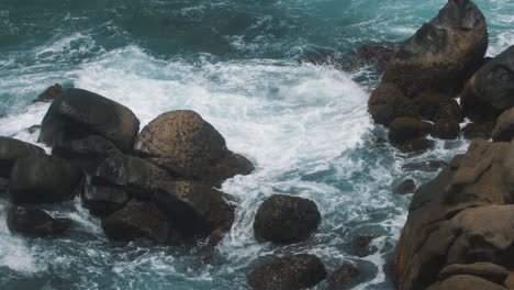 slow-motion shot of blue water and waves crashing against a stack of rocks on a cliff, taken in tayrona park, colombia