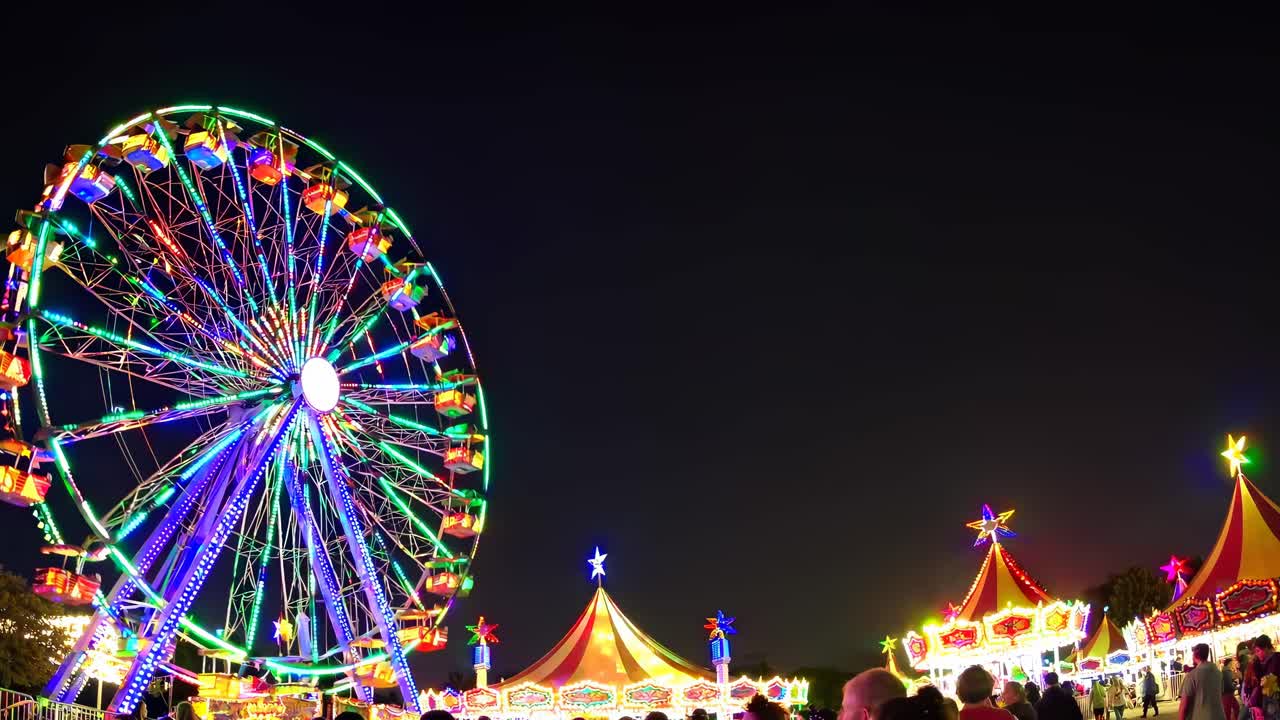 Nighttime carnival scene with a low-angle view of a vibrant Ferris wheel and colorful tents