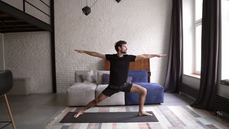 el hombre practica la postura del guerrero de yoga en su propia sala de estar en el tapete