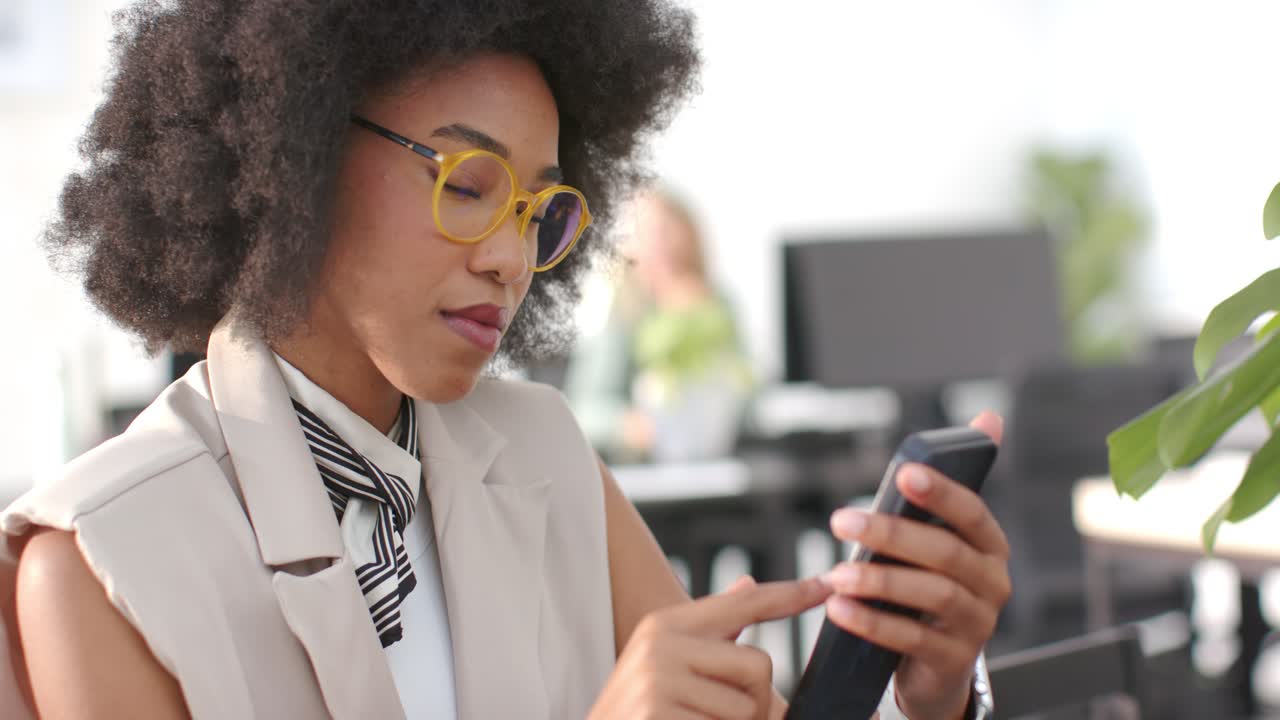 Female team seeing African American woman using smartphone, tapping and smiling at camera in office