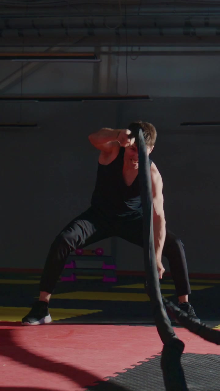 Atlet trener med battle ropes på treningsstudio. Intenst fokus, kraftfull bevegelse, svette synlig. Ideell for trening, styrketrening eller treningsrelaterte temaer
