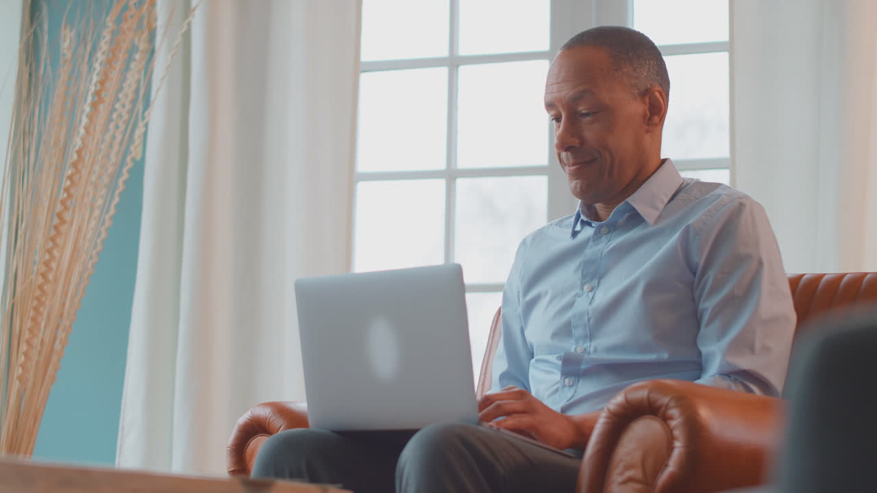 Mature Man Or Businessman Working From Home Sitting In Armchair Using Laptop Computer