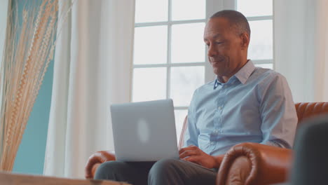 mature man or businessman working from home sitting in armchair using laptop computer