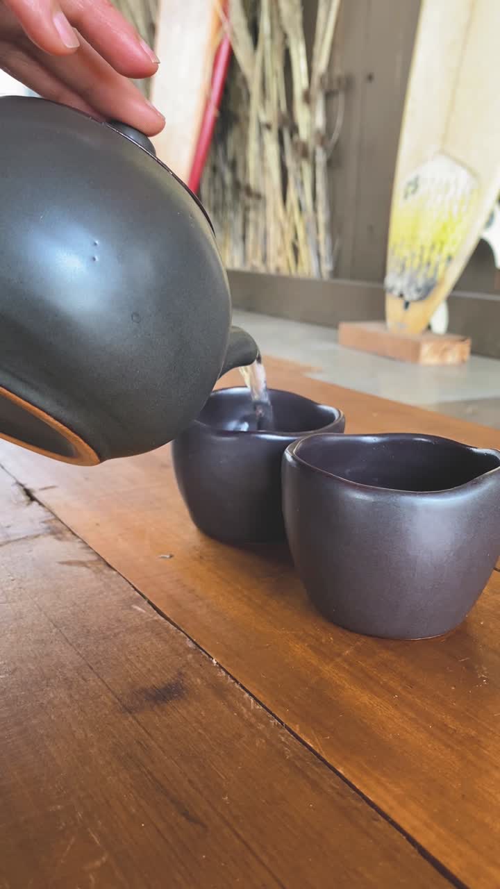 Primo piano di una mano che versa il tè da una teiera in una tazza di ceramica su un tavolo di legno