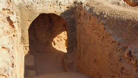 sunlit stone steps descend into an arched entrance carved from rock at tombs of the kings in paphos, cyprus. high angle shot