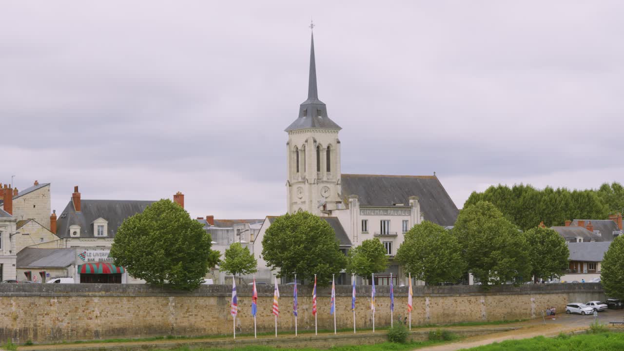 vista de un hermoso antiguo edificio histórico de la iglesia con aguja en saumur, francia con banderas alineadas a la orilla del río loira