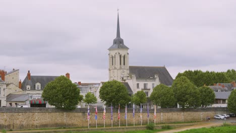 view of beautiful old historic church building with spire in saumur, france with flags lining riverside of loire