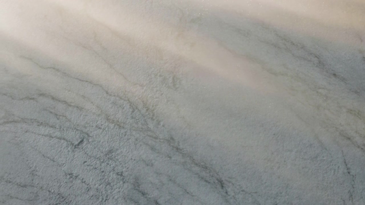Nærbillede af en lysegrå marmoroverflade med fine årer og et blødt diagonalt lysbånd, der skaber en rolig neutral baggrund med en elegant finish.
