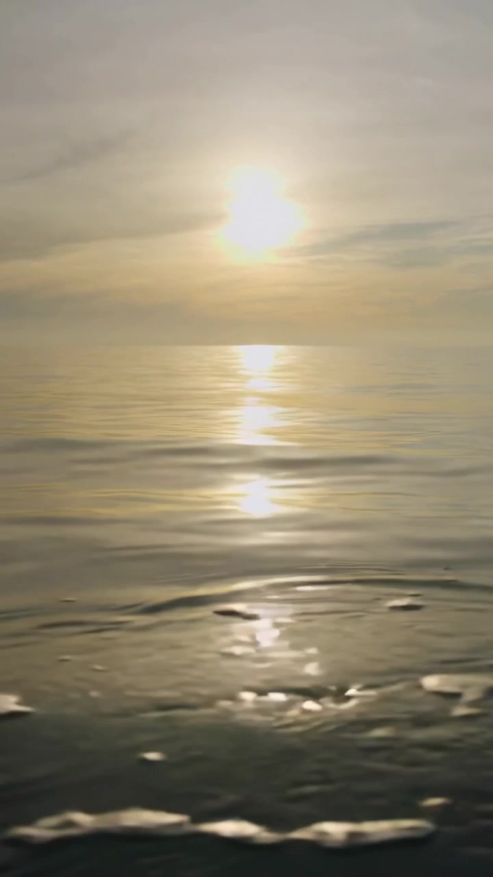 Vertical video: Recording low cam capturing sun vertical reflection across sea, foam, sunrise glow