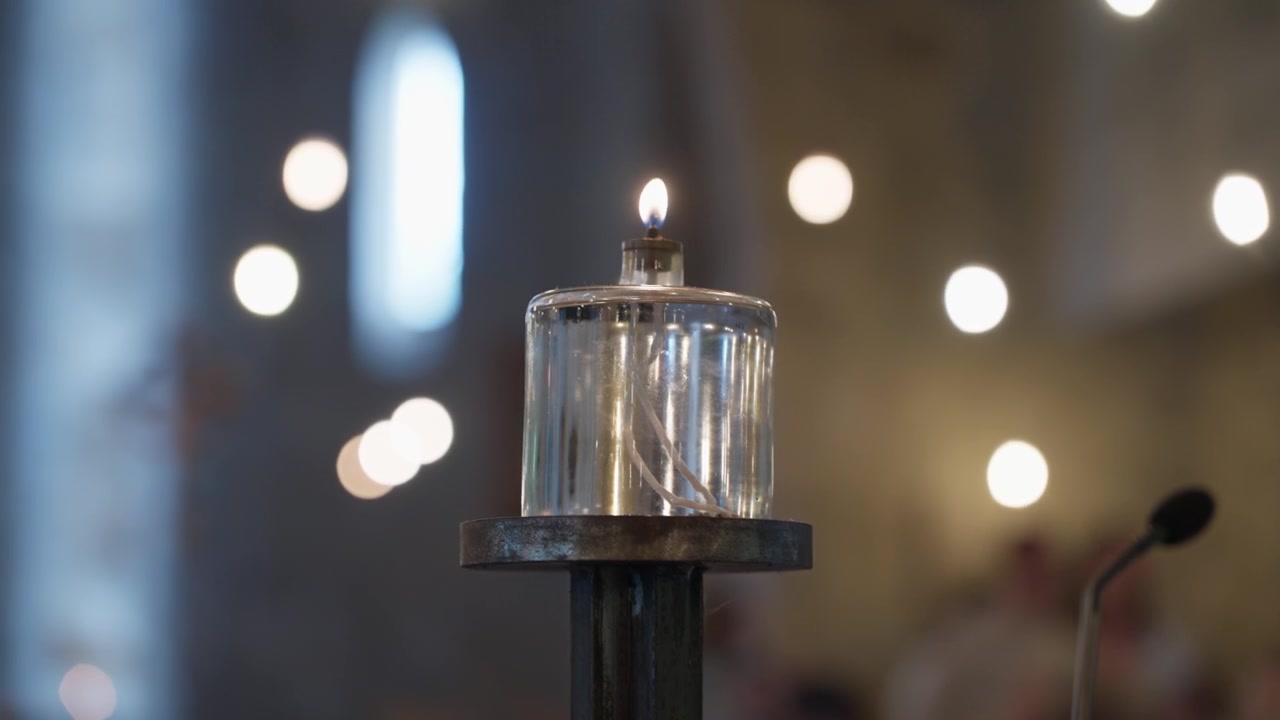 Glass oil candle burning on metal stand inside church with bokeh lights