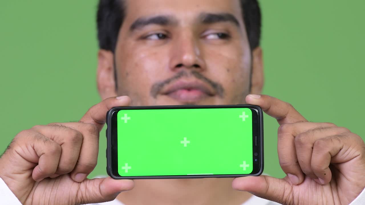 젊은 잘생긴 페르시아인 남자가 전화를 보여줍니다.