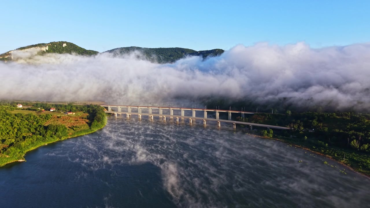 早朝の光の中、霧が川を覆い、橋が陸地をつないでいます。