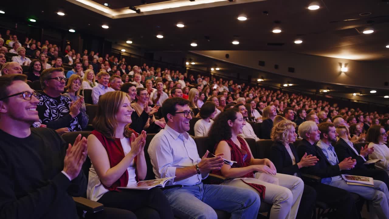 Wide-angle shot of a large audience seated in a theater, attentively watching a presentation
