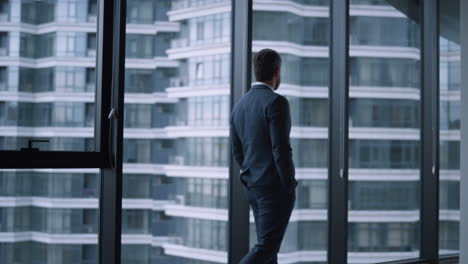 Executive-man-walking-office-alone.-Young-businessman-standing-looking-window.