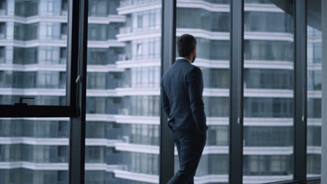 executive man walking office alone. young businessman standing looking window.