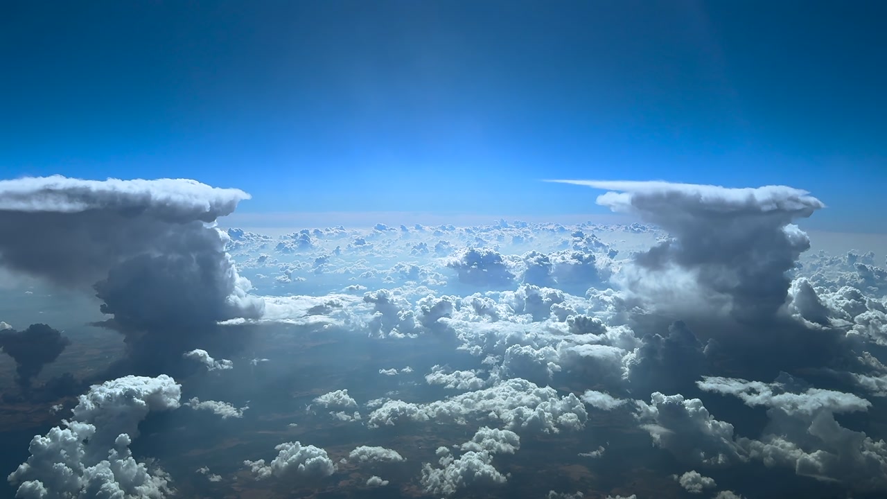 An immersive cockpit view from the cockpit of a jet flying between two storm clouds under a blue and bright sky in a sunny day.