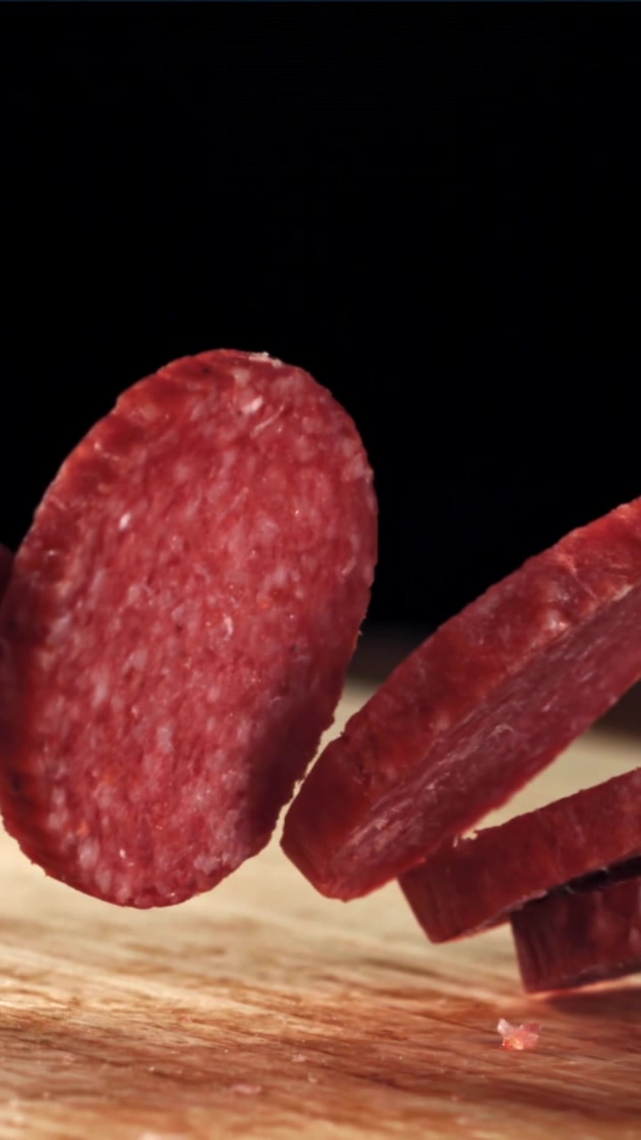 Fette di salame che cadono su un tagliere di legno al rallentatore