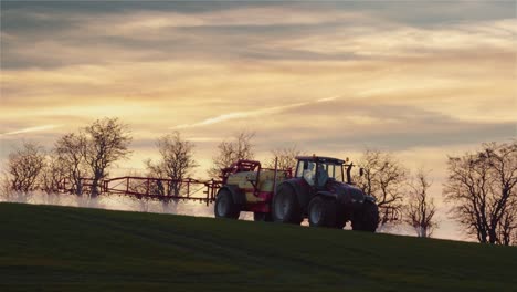 un agricultor con un tractor rociando productos químicos en un campo durante la puesta de sol