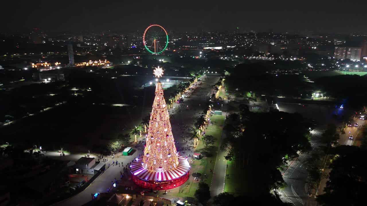 Beautiful illuminated Christmas tree filmed through an orbital drone movement, with a Ferris wheel in the background and a lovely park in the city of São Paulo