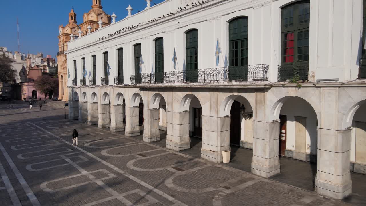 Aerial pan shot capturing quiet square and Cordoba Cabildo colonial town hall with iconic arch passageway at San Martin plaza in downtown city