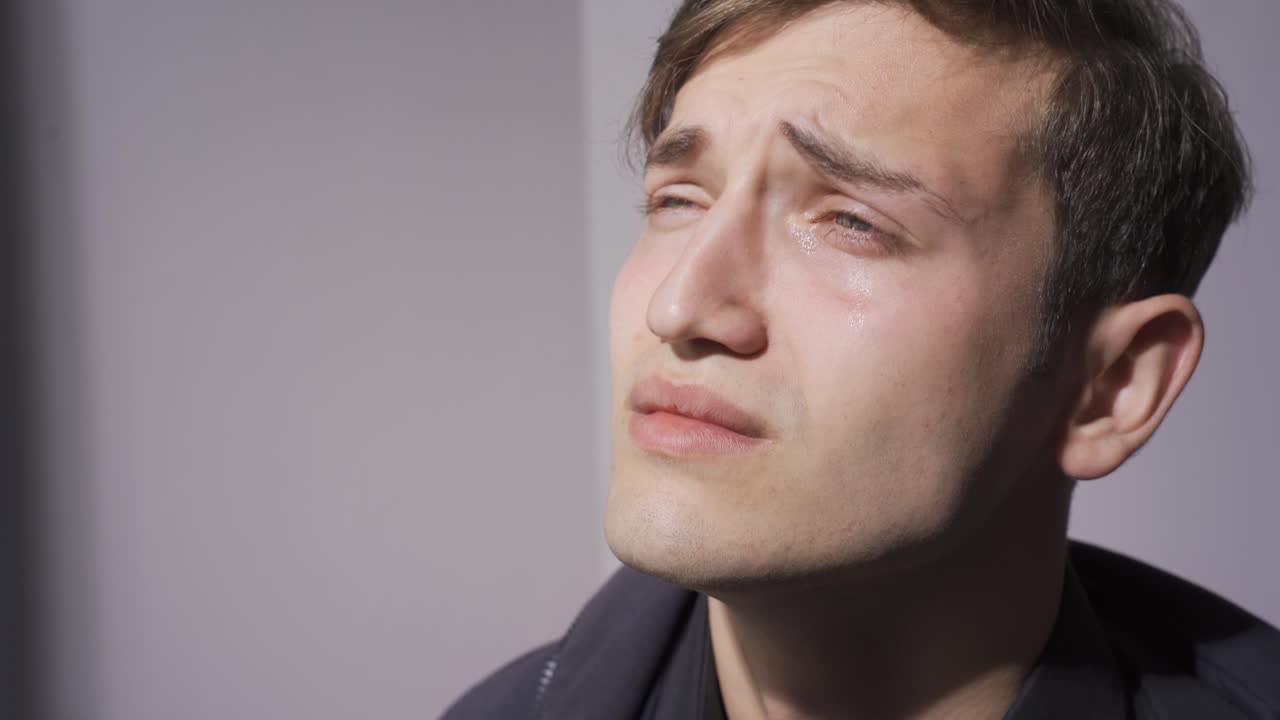 우울한 젊은 매력적인 남자가 울고 있습니다.