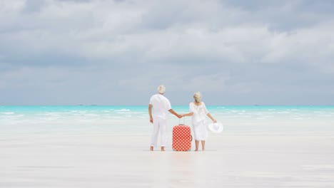 barefoot mature caucasian couple on beach with suitcase