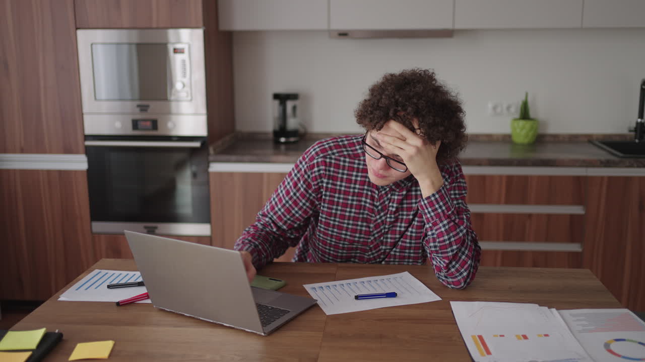 estudiante de cabello rizado atractivo joven con gafas está estudiando en casa usando una computadora portátil escribiendo en un cuaderno. estudiante universitario usando una computadora portátil viendo un seminario de aprendizaje en línea a distancia