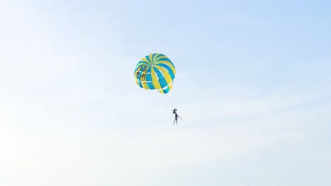 a parasailer glides through the sky over karon beach, phuket. bright daylight enhances the vibrant parachute against a clear blue sky