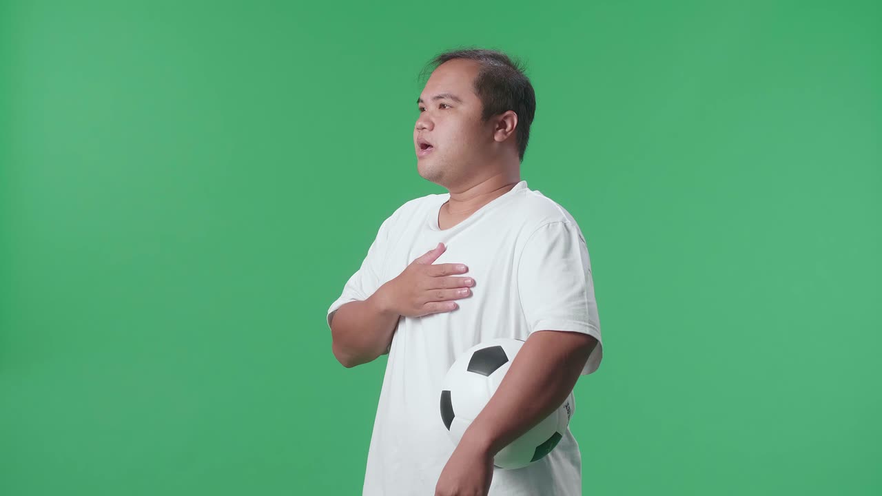 초록색 스크린 배경 에서 축구 를 응원 하는 동안 공 을 들고 국악 을 부르는 아시아인 의 측면 시각