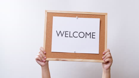 woman's hand shows the paper on board with the word welcome in white studio background with copy space.