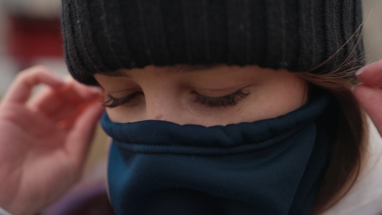 마스크를 조절하는 여성을 클로즈업한 사진, 보호 장비를 섬세하게 조절하는 여성과 도시 배경, 도시 환경 속에서 조심스럽게 마스크 위치를 잡는 여성의 상세한 스냅 사진