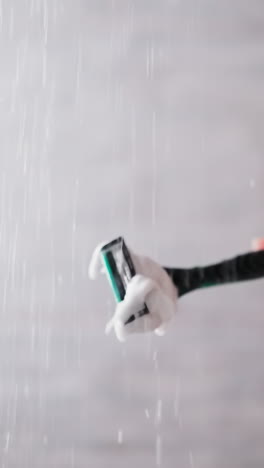 woman cleans razor from foam in shower sprays closeup. lady holds shaver under falling down water jets to wash out froth in bathroom. shaving tool