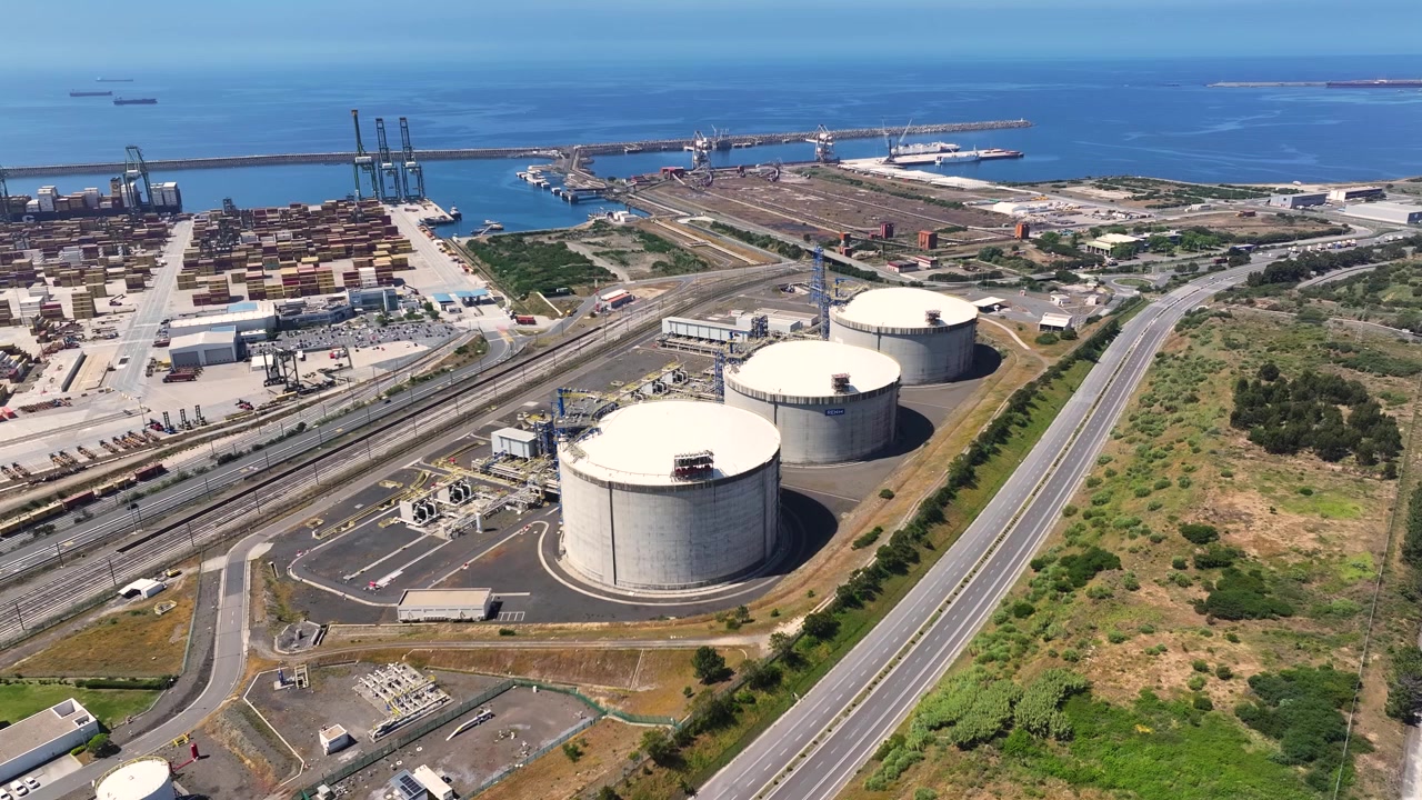 Vista aerea di un terminale GNL con serbatoi multipli di stoccaggio del gas. L'area industriale vicina include navi e infrastrutture energetiche. Focus su fornitura e stoccaggio di gas naturale