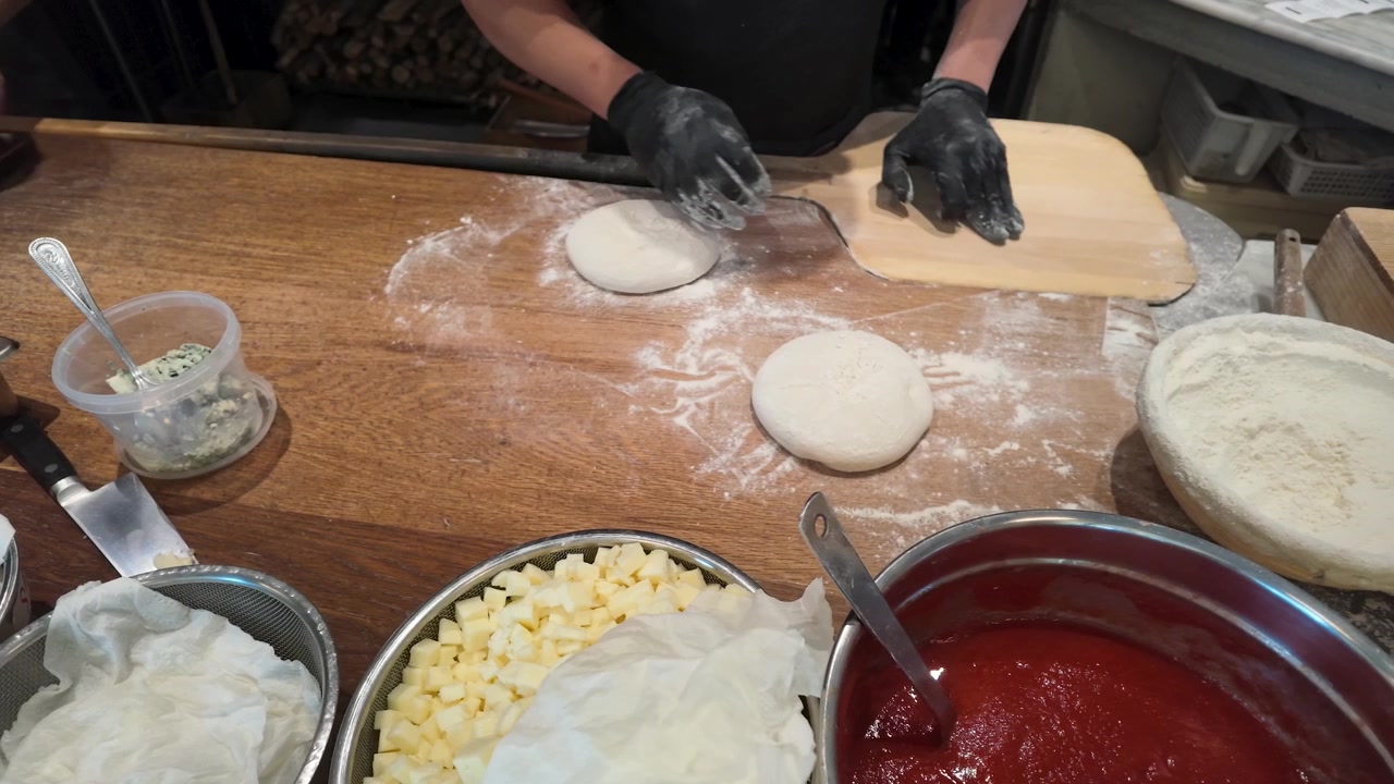 Ripresa dall'alto di uno chef con guanti neri che prepara l'impasto della pizza con farina e ingredienti