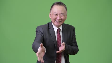 mature sketchy japanese businessman giving handshake against green background