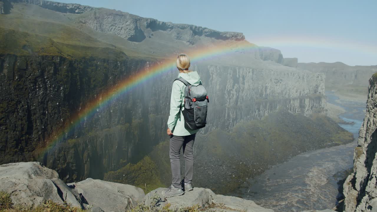 mujer de pie en el borde de un acantilado mirando hacia el cañón con el río cerca de la cascada de detifoss en islandia