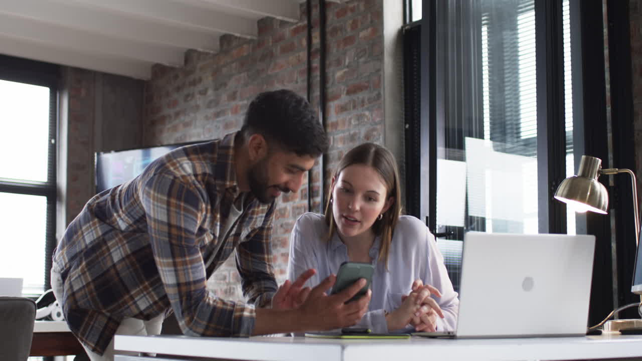 Young Caucasian woman and young Asian man are focused on a laptop screen in a business office
