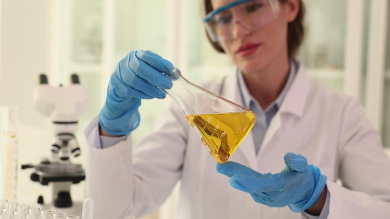 Female scientist analyzing a yellow liquid in a flask in a laboratory
