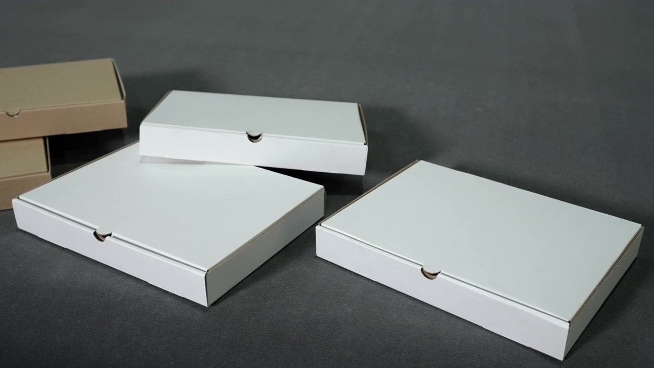 Four flat takeaway-style cardboard containers with white lids and kraft brown sides sit on dark matte background, cleanly lit for shipping, retail, storage, and product presentation use