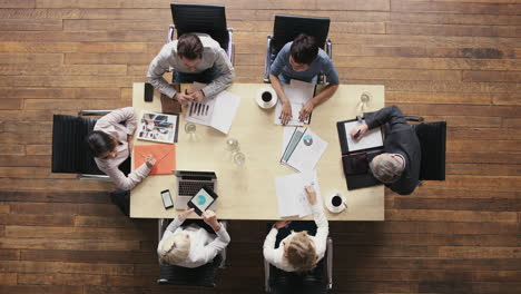 Vista-Superior-Diversos-Empresarios-Reunidos-En-La-Mesa-De-La-Sala-De-Juntas-Discutiendo-El-Informe-Financiero