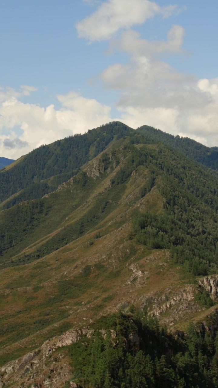 Ampia inquadratura di una cresta montuosa verde e pendii rocciosi sotto un cielo blu con nuvole nella valle di Ak-Kem, Repubblica dell'Altai, Russia, serena scena di viaggio nella natura selvaggia