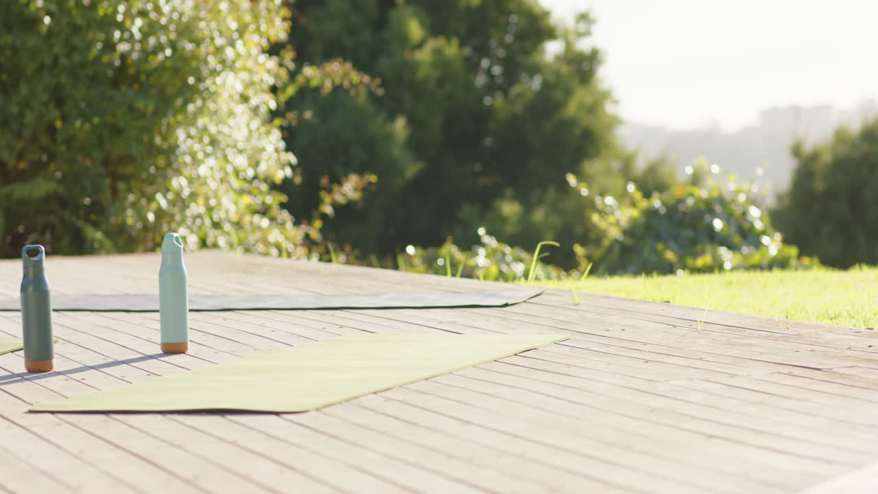 Camera moving forward showing two reusable bottles between two yoga mats on deck, framing practice