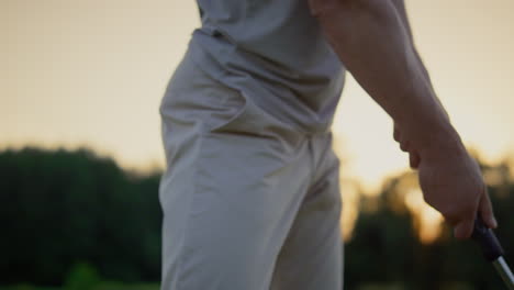 golfer hand swinging club putter on sunset golf course. man hitting ball outside