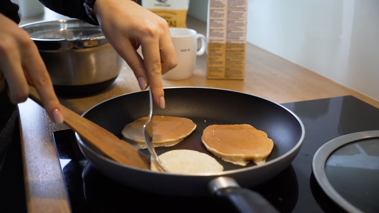 el primer plano de una mujer girando panqueques en la sartén en la cocina de casa, la mujer está haciendo el desayuno