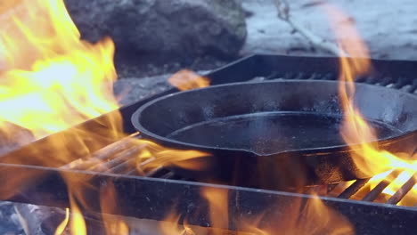 oiled cast iron pan placed onto open fire grill to season the utensil