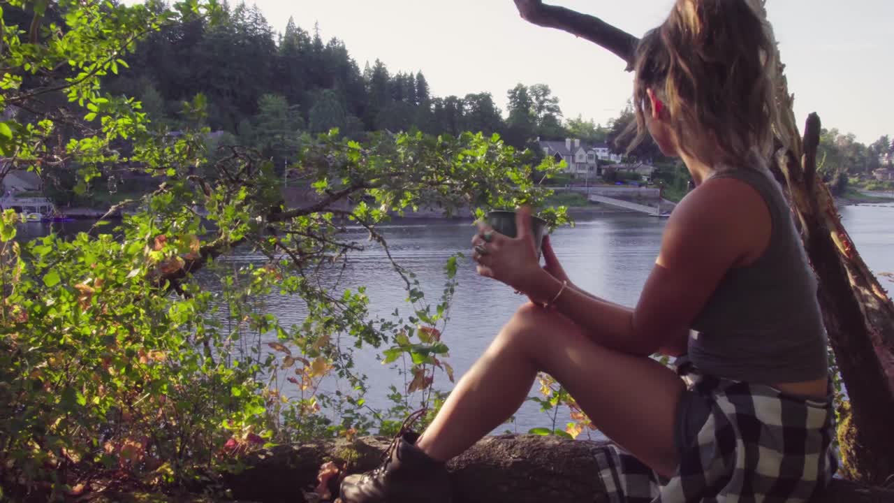 Süßes Hipster-Mädchen sitzt an einem See mit einer Tasse zum Trinken und Entspannen