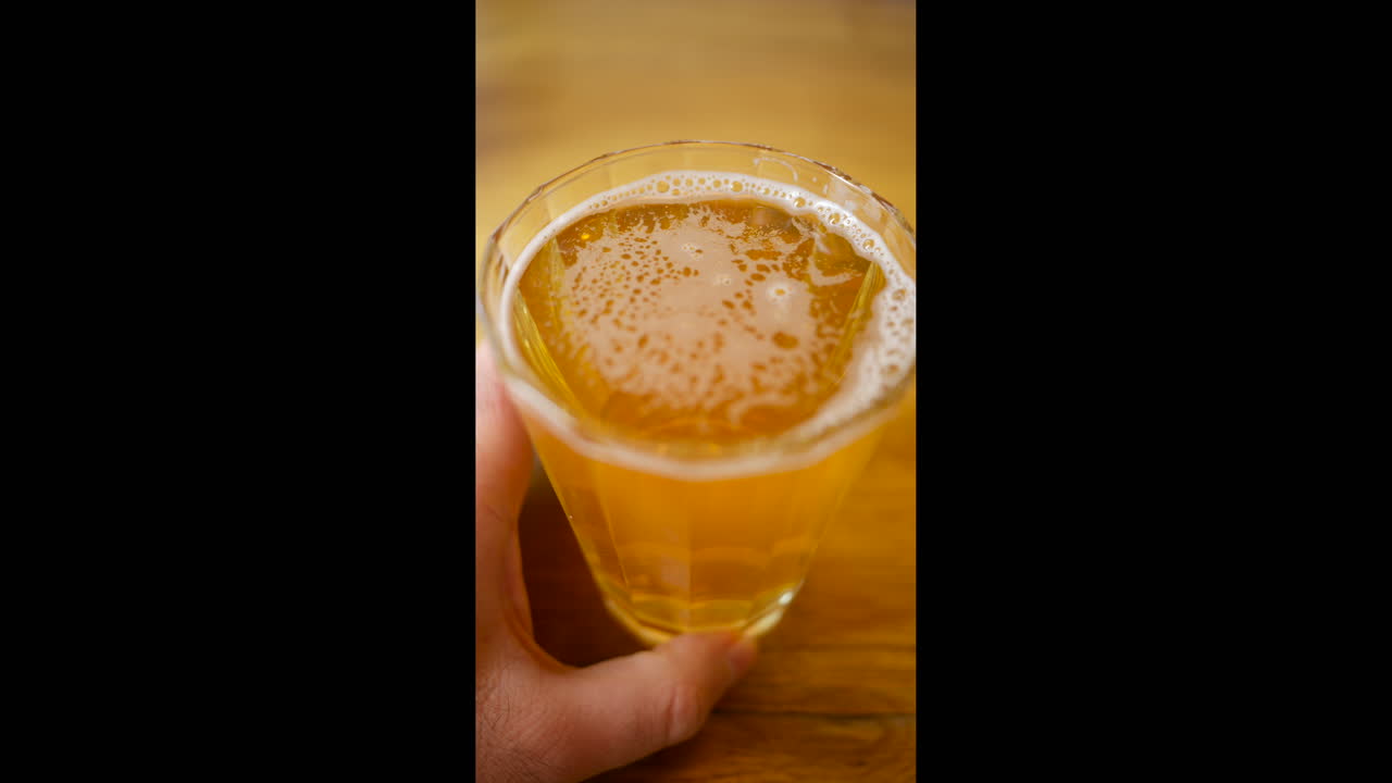 Vista dall'alto di un bicchiere di birra lager chiara appena versato, con bolle di schiuma, su un tavolo di legno. Verticale.