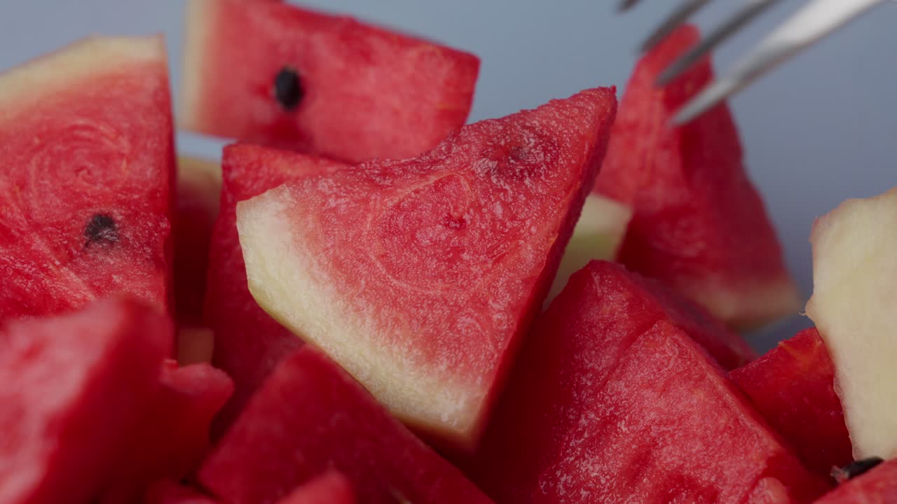 A fork picking a fresh watermelon slice from a bowl of juicy red cubes in close-up view