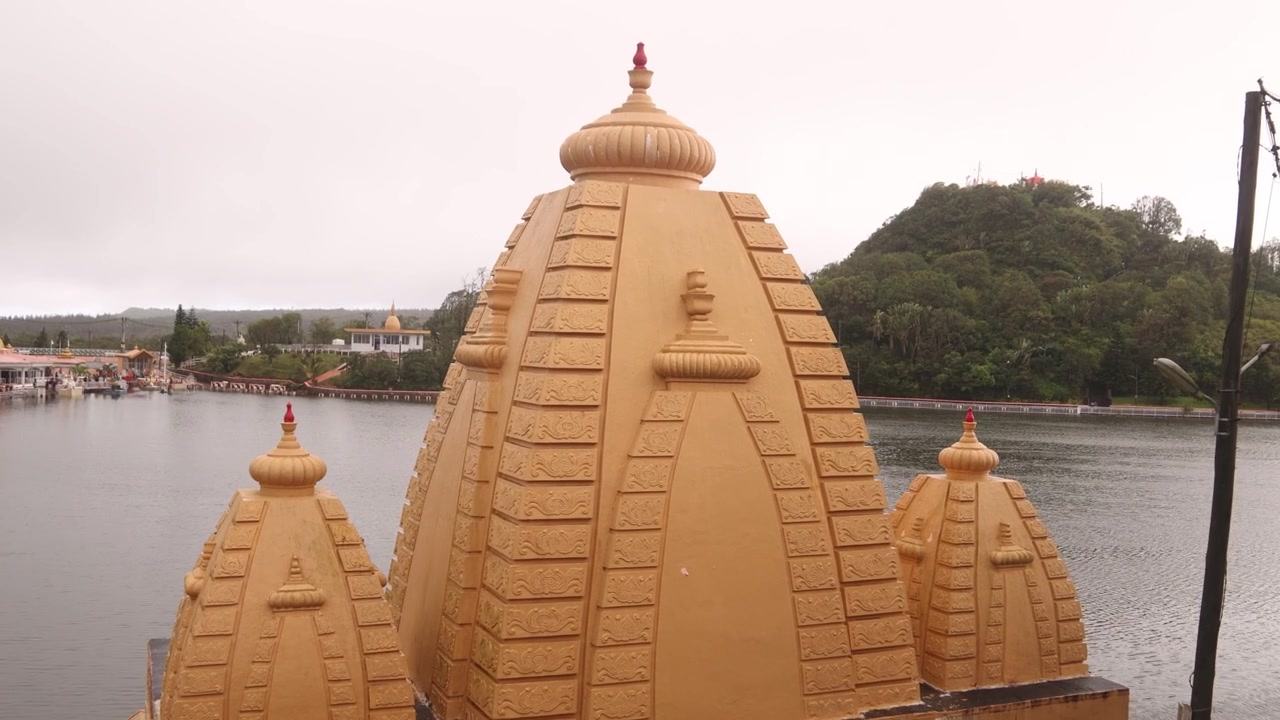 Scatto ravvicinato delle guglie dorate del tempio a Ganga Talao, Mauritius. L'architettura sacra si erge sopra il sereno lago vulcanico, un importante sito di pellegrinaggio indù nel cuore montuoso dell'isola